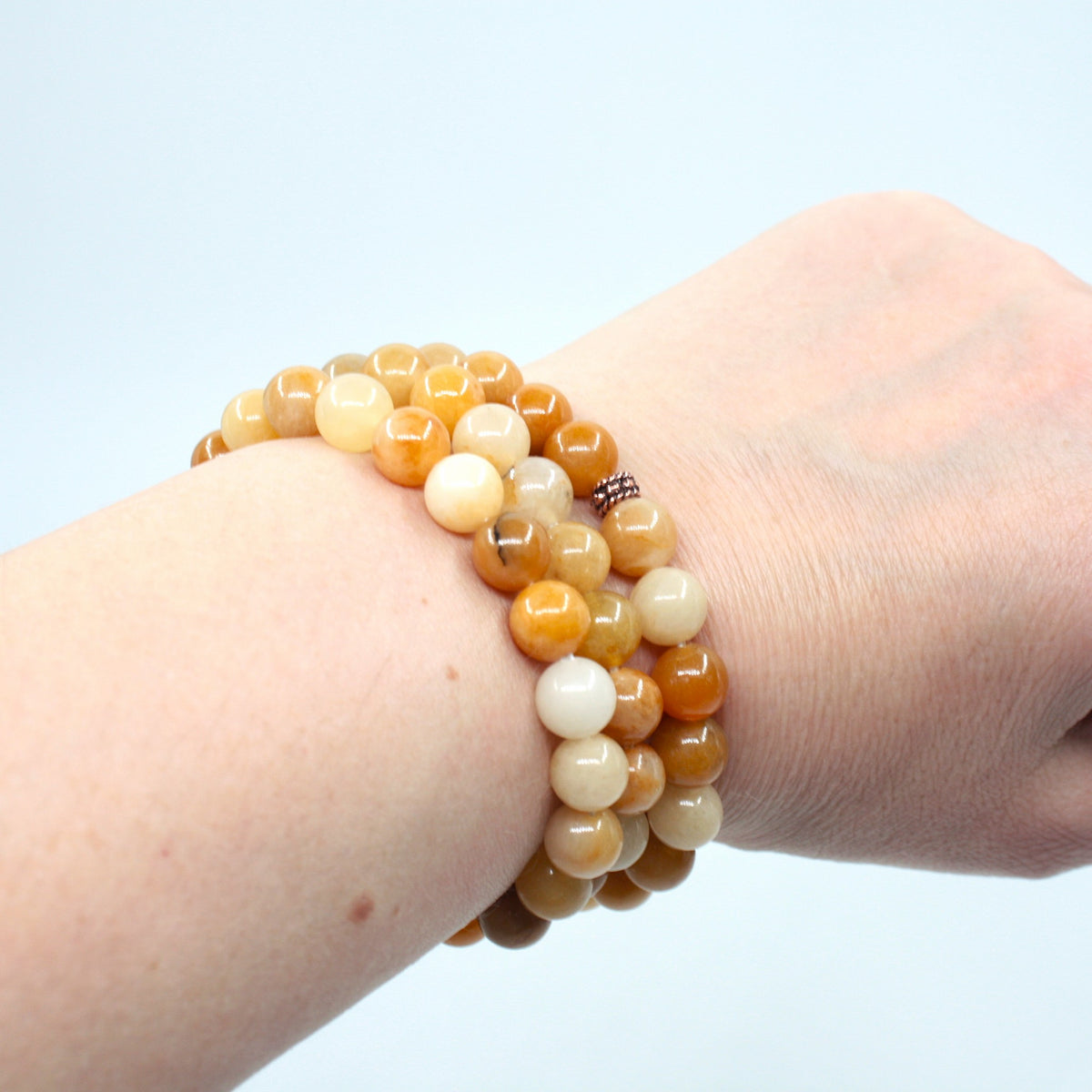 Kolme keltainen jade rannekorua ranteessa. Tausta on valkoinen. Three yellow jade bracelets on the wrist. Background is white.