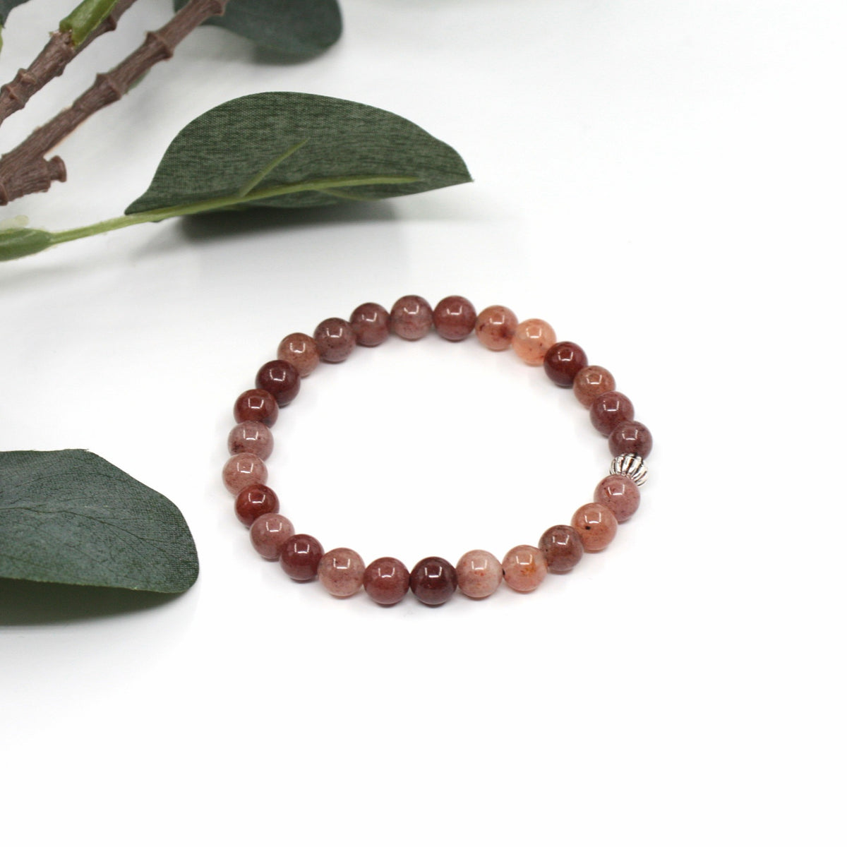 Aventuriini rannekoru valkoisella alustalla. Vasemmalla puolella vihreitä lehtiä. Aventurine stretchy bracelet on the white surface. Left side is green leaves.