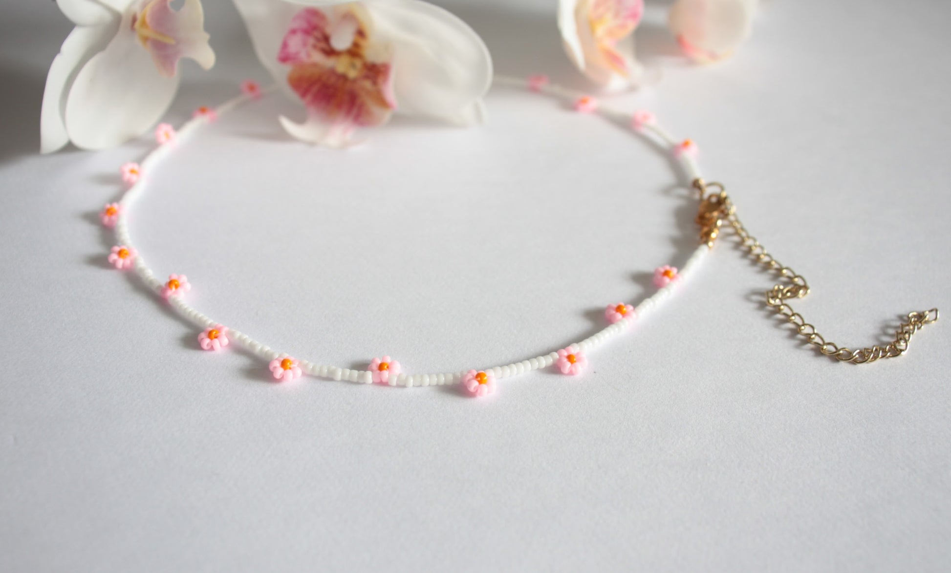 Daisy chain choker necklace white with pink and orange flowers. Päivänkakkara daisy chain choker kaulakoru valkoinen vaaleanpunaisilla kukilla. Kukkien keskusta on oranssi.