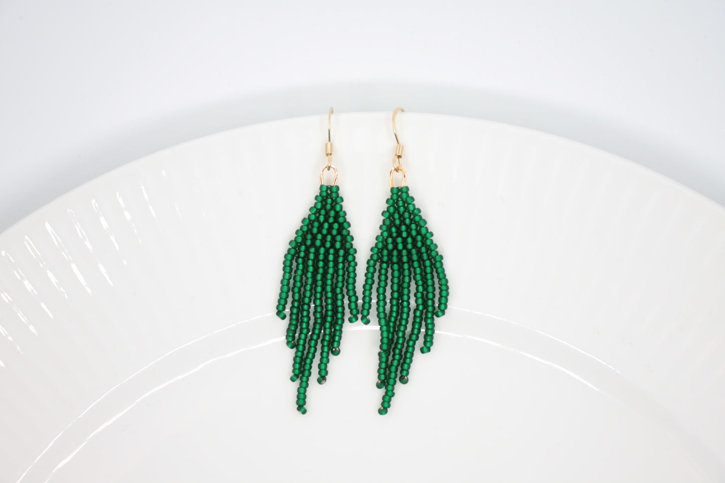 Hapsulliset helmikorvakorut valkoisella alustalla. Korvakorujen väri on matta vihreä. Seed bead fringe earrings on white background. Earrings color is matte green