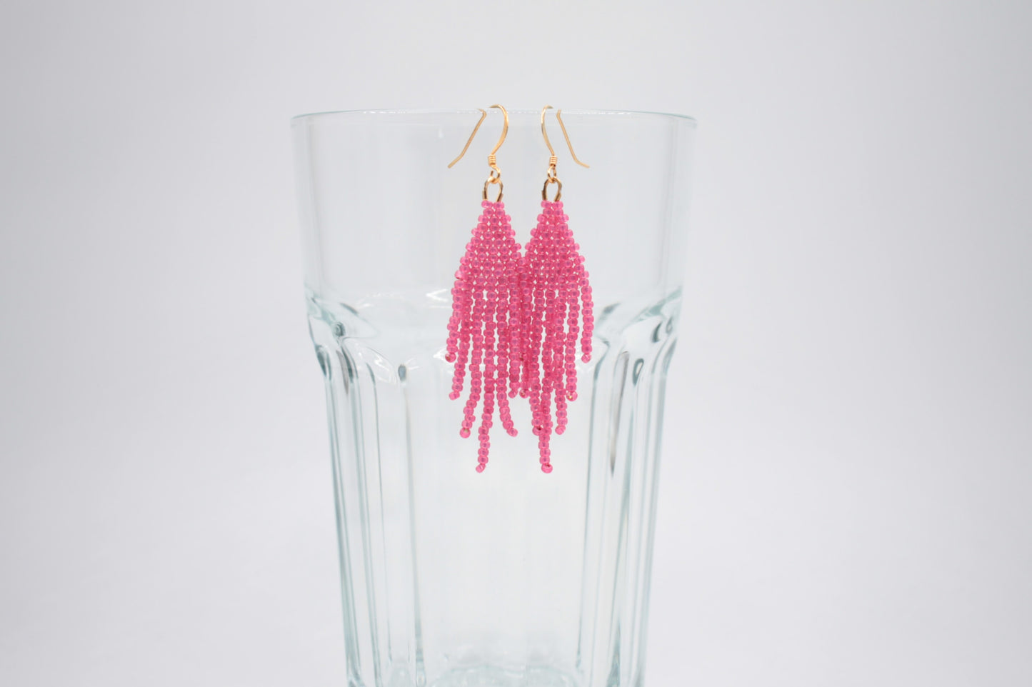 Roikkuvat hapsulliset helmikorvakorut värinä kimalteleva vadelma valkoisella taustalla. Seed bead fringe earrings sparkling raspberry- colored on the white background.