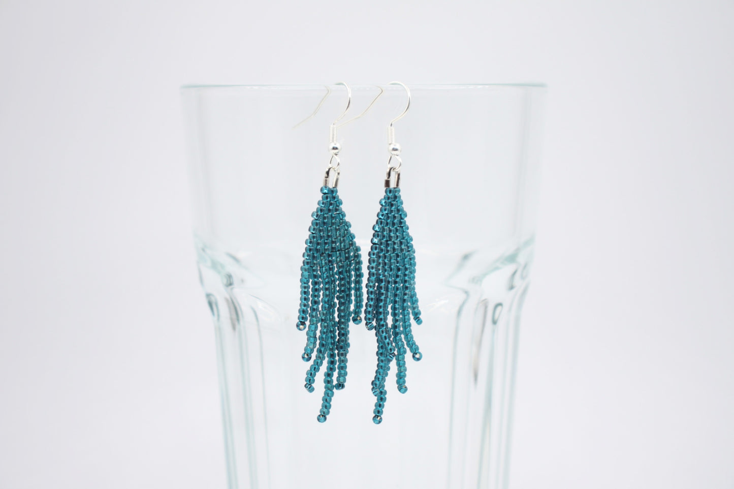 Sinisen safiirin väriset roikkuvat hapsulliset helmikorvakorut valkoisella alustalla. Seed bead fringe earrings blue sapphire-coloured on white background.