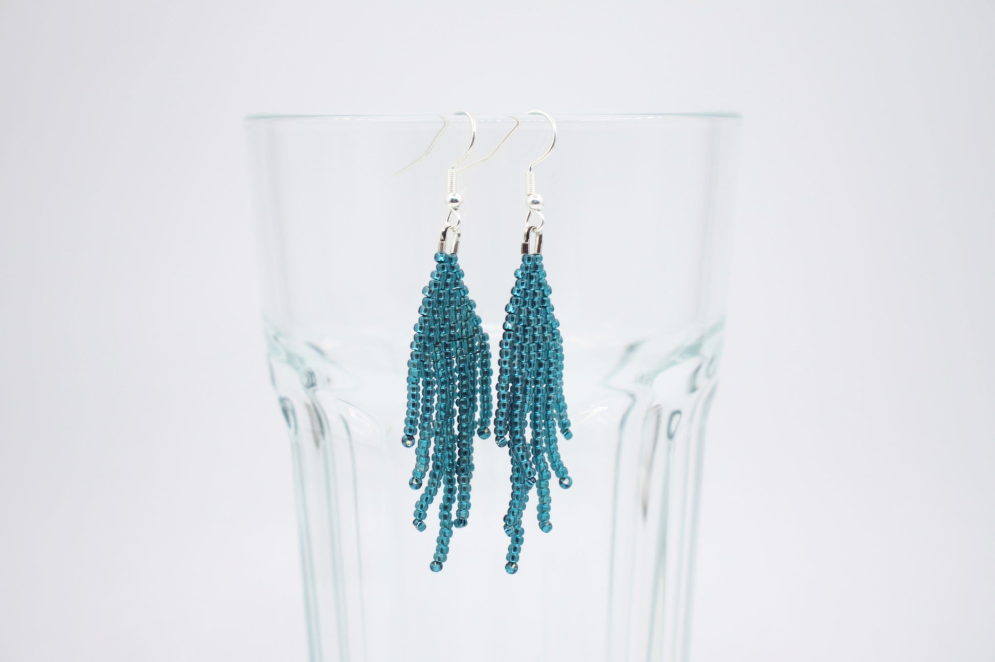 Sinisen safiirin väriset roikkuvat hapsulliset helmikorvakorut valkoisella alustalla. Seed bead fringe earrings blue sapphire-coloured on white background.