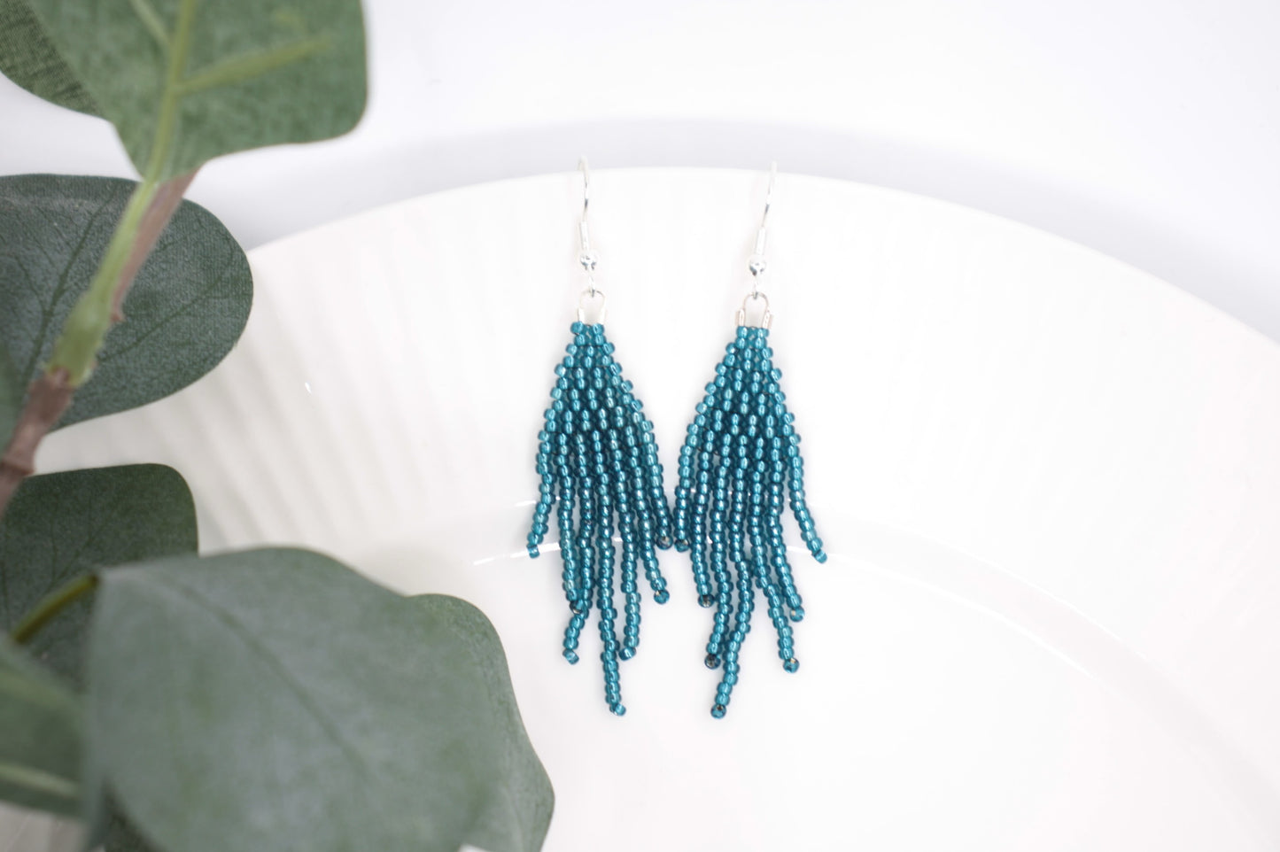 Sinisen safiirin väriset roikkuvat hapsulliset helmikorvakorut valkoisella alustalla. Seed bead fringe earrings blue sapphire-coloured on white background.