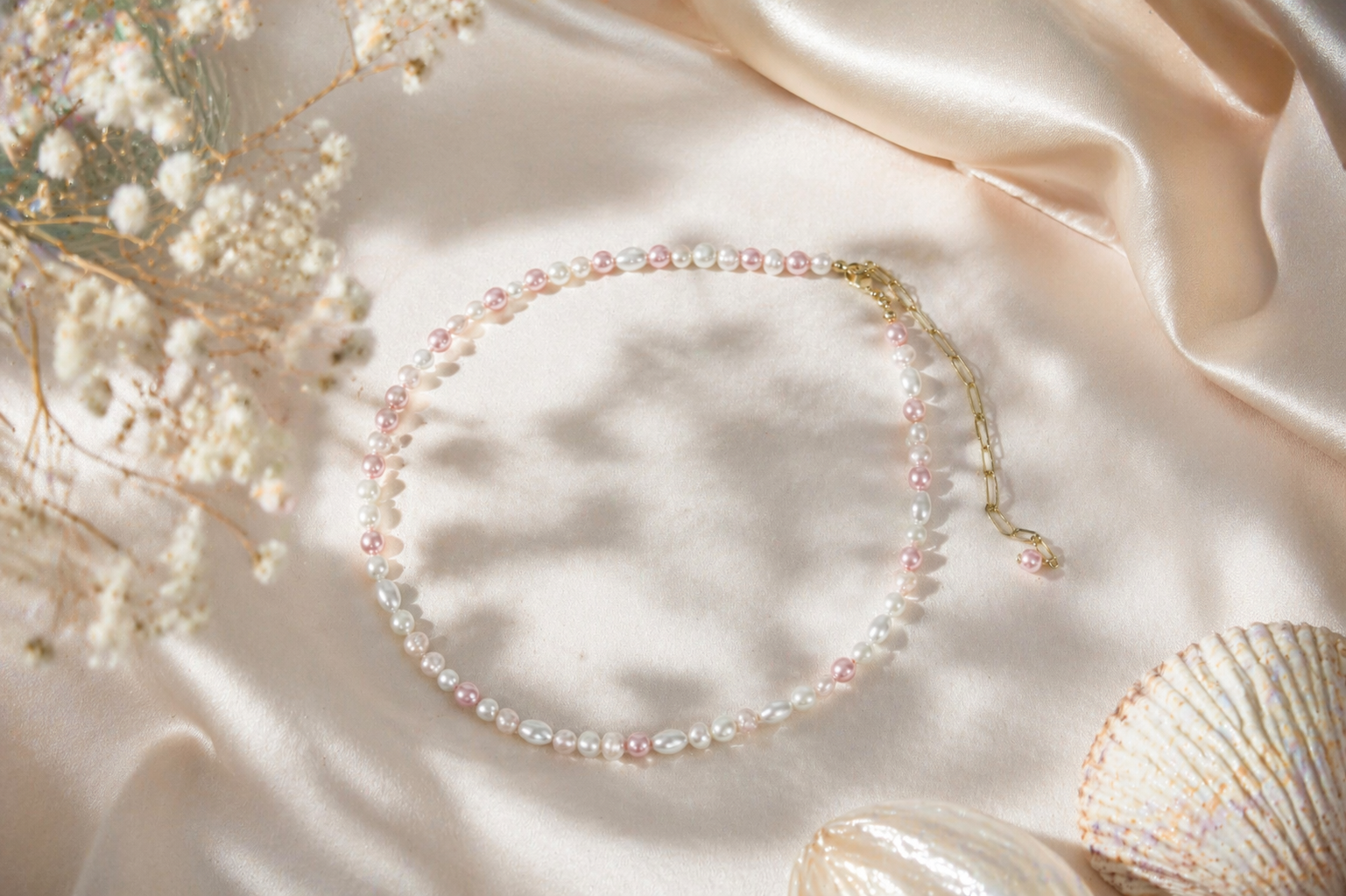 Handmade freshwater pearl necklace with pink and white glass beads and gold extension chain on soft neutral fabric background. Käsintehty makeanvedenhelmikaulakoru vaaleanpunaisilla ja valkoisilla lasihelmillä sekä kullanvärisellä jatkoketjulla vaalealla kangastaustalla.
