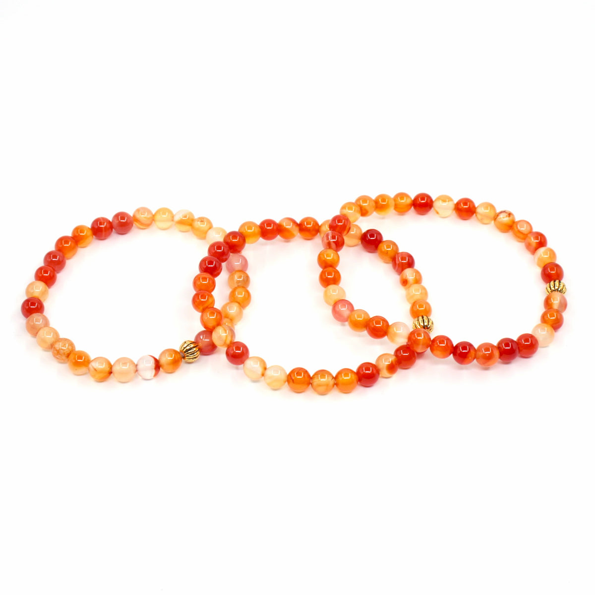 Kolme karneoli rannekorua valkoisella alustalla. Three carnelian bracelets on a white surface.