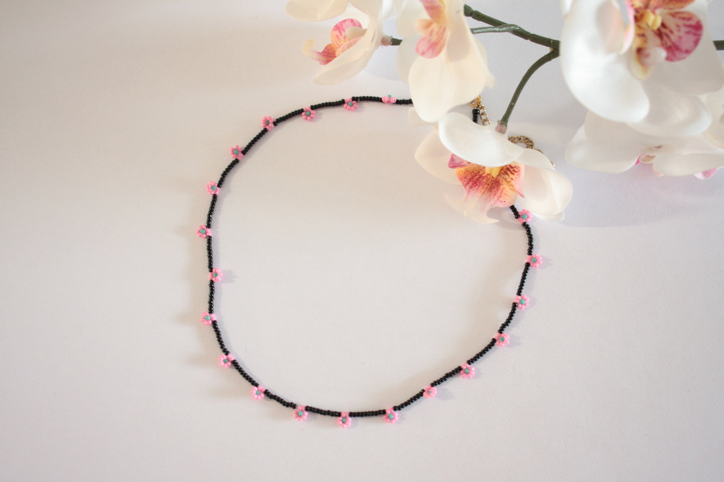Daisy chain choker necklace black with pink and green turquoise flowers. Päivänkakkara daisy chain choker kaulakoru musta vaaleanpunaisilla kukilla. Kukkien keskusta on vihreäturkoosi.