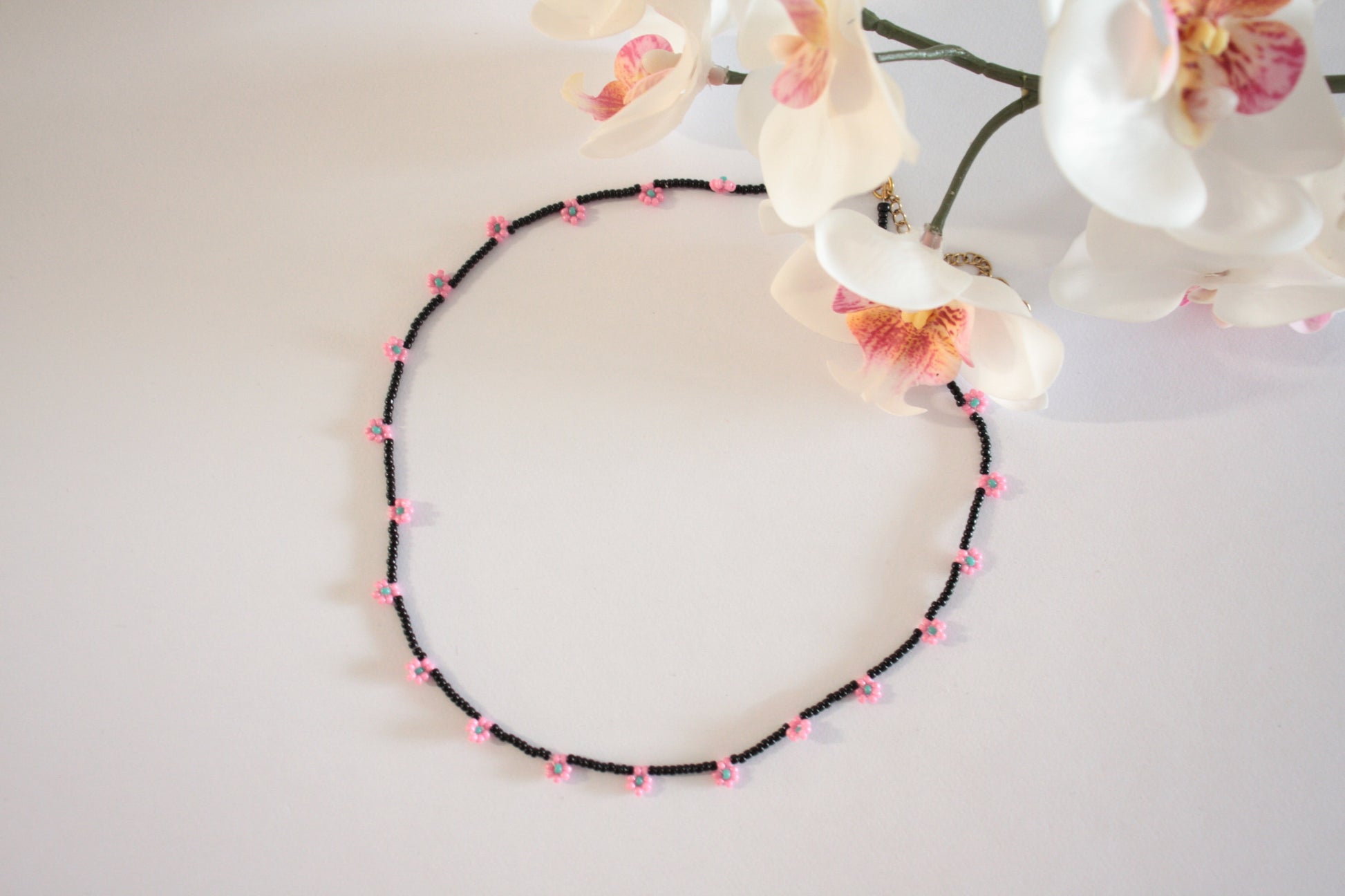 Daisy chain choker necklace black with pink and green turquoise flowers. Päivänkakkara daisy chain choker kaulakoru musta vaaleanpunaisilla kukilla. Kukkien keskusta on vihreäturkoosi.