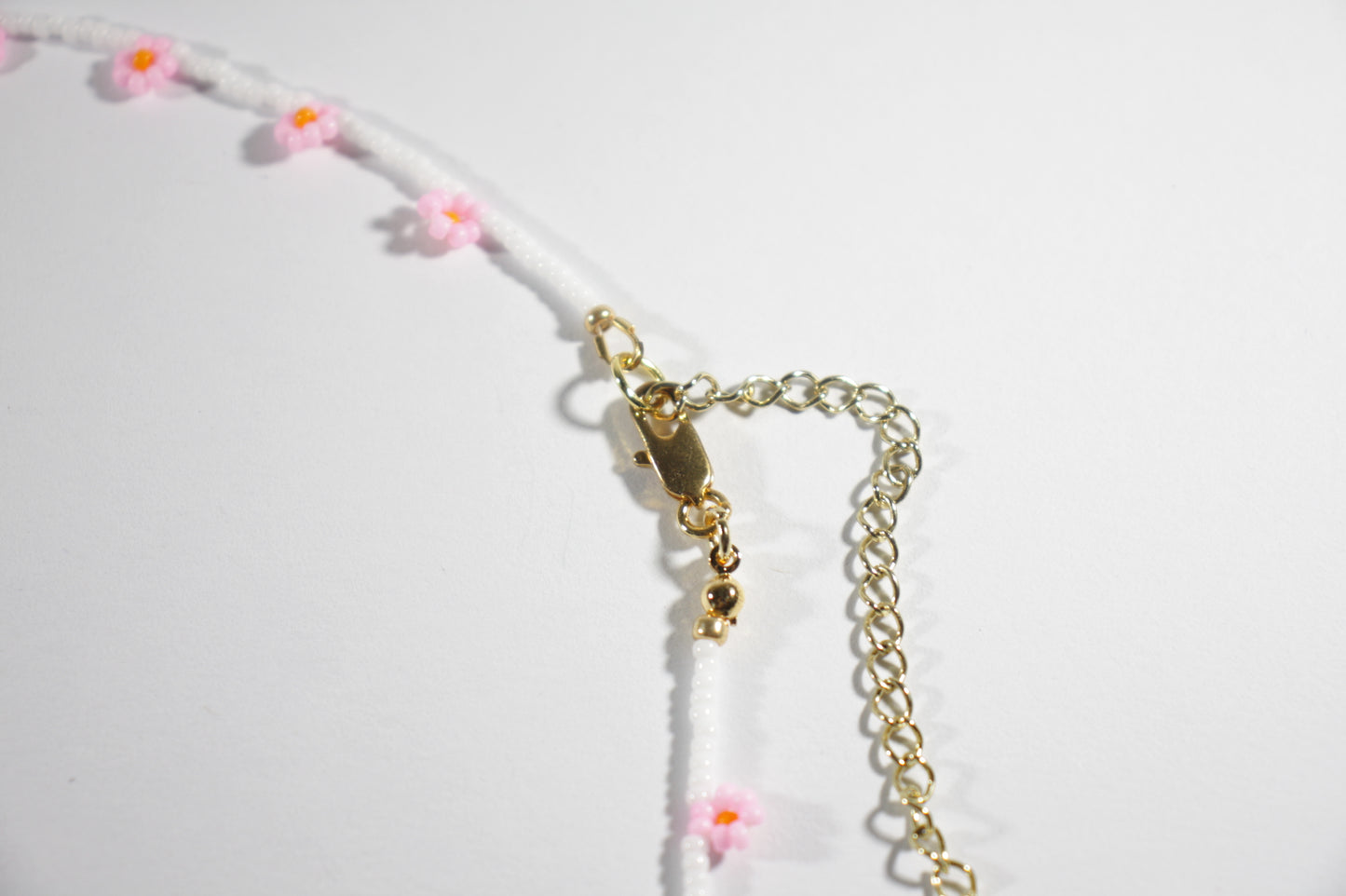 Daisy chain choker necklace white with pink and orange flowers. Päivänkakkara daisy chain choker kaulakoru valkoinen vaaleanpunaisilla kukilla. Kukkien keskusta on oranssi.