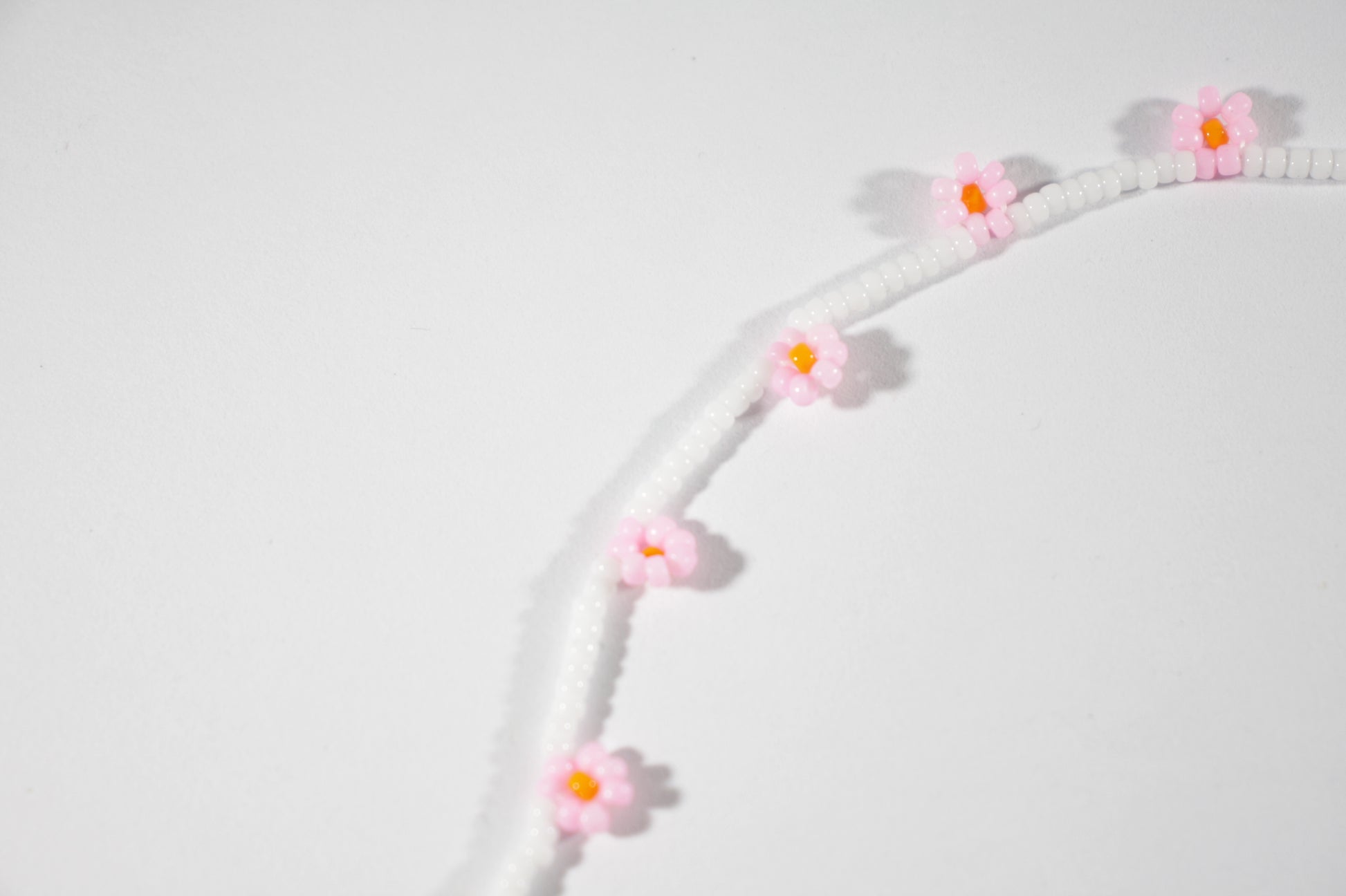 Daisy chain choker necklace white with pink and orange flowers. Päivänkakkara daisy chain choker kaulakoru valkoinen vaaleanpunaisilla kukilla. Kukkien keskusta on oranssi.