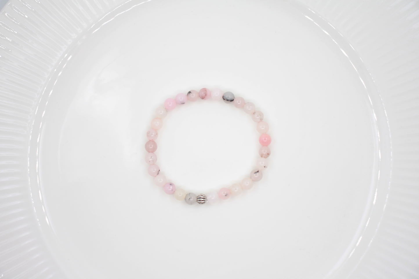 Jaspis kivihelmirannekoru vaaleanpunainen valkoisella alustalla. Pink jasper stone bead bracelet on a white surface. 
