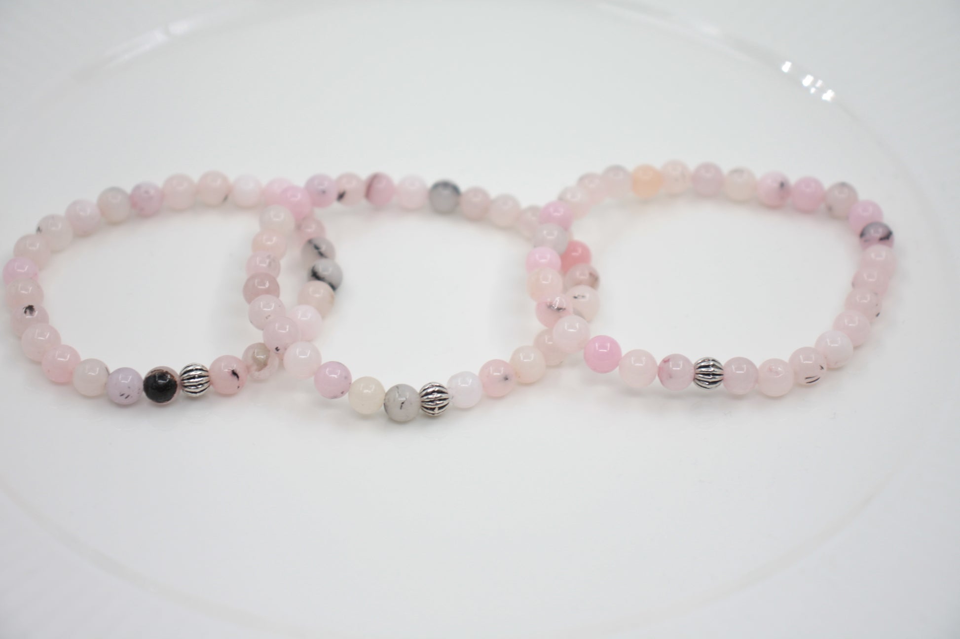 Jaspis kivihelmirannekoru vaaleanpunainen valkoisella alustalla. Pink jasper stone bead bracelet on a white surface. 