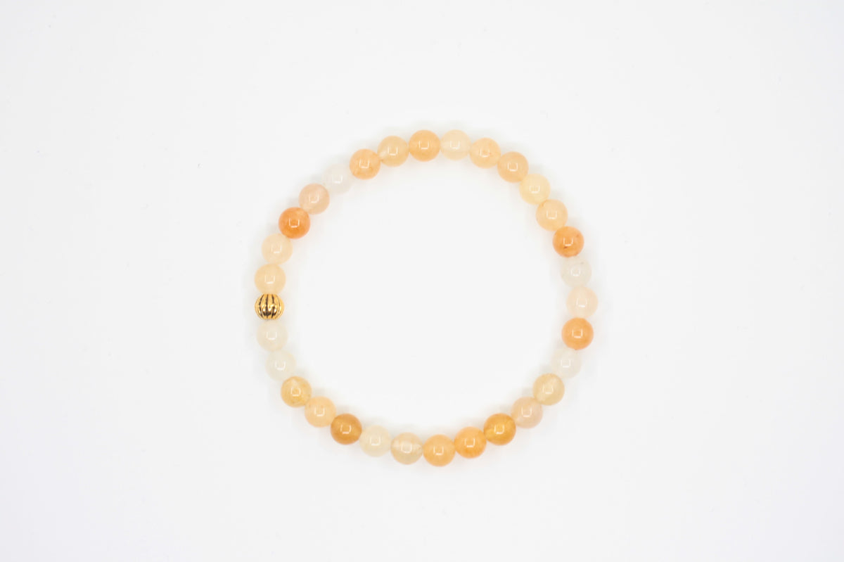 Keltainen jade joustava rannekoru kullan värisellä helmellä valkoisella alustalla. Yellow jade stretchy bracelet with gold color metal bead. Bracelet is on white background.