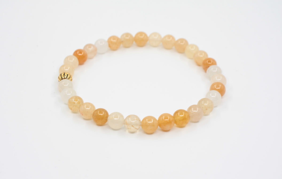 Keltainen jade joustava rannekoru kullan värisellä helmellä valkoisella alustalla. Yellow jade stretchy bracelet with gold color metal bead. Bracelet is on white background.