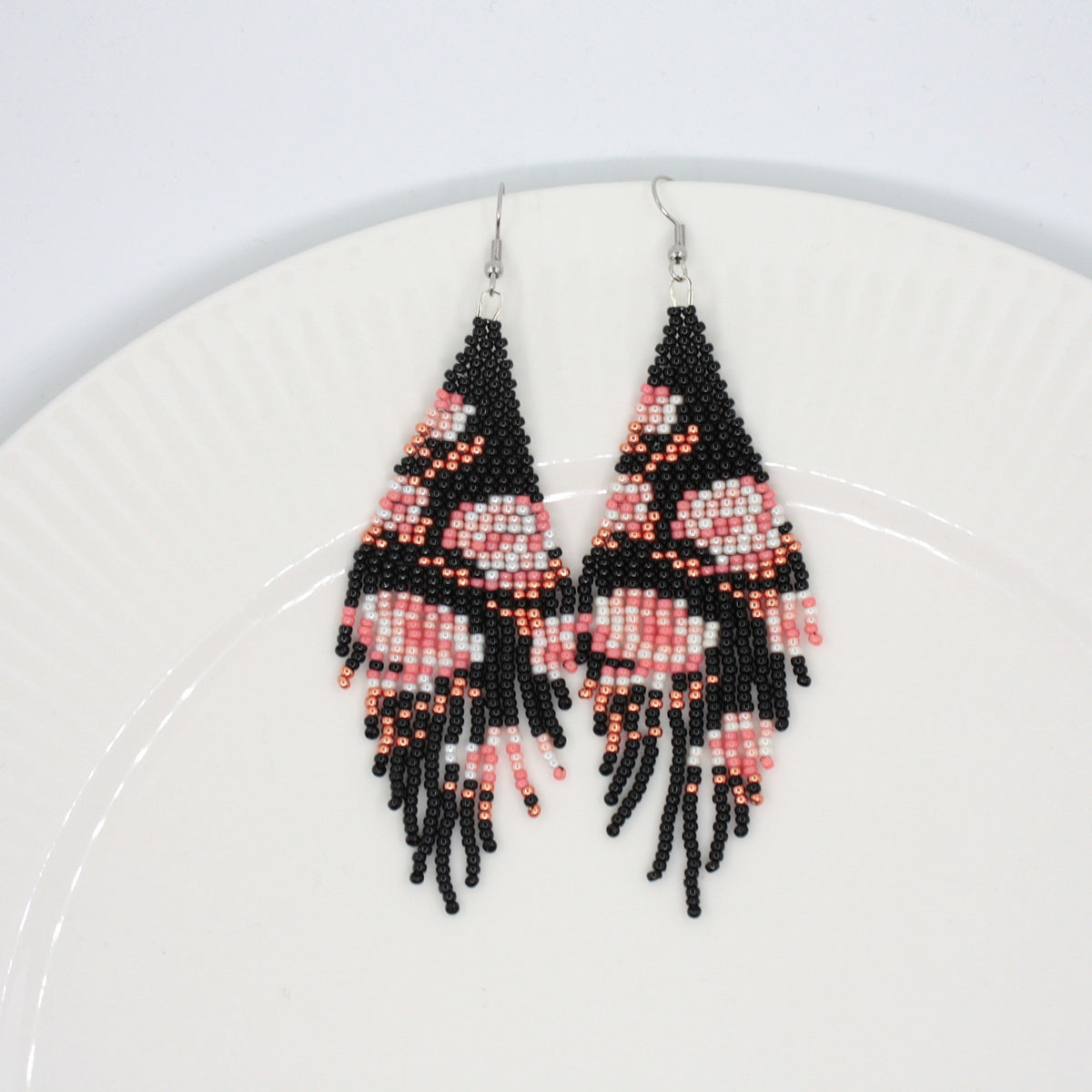 Long beaded seed bead fringe earrings on white plate. Base color of these earrings is and black and it has pink roses pattern. Pitkät käsintehdyt roikkuvat helmikorvakorut valkoisella lautasella. Pohjaväri näissä korvakoruissa on musta sekä, kuviona on pinkin sävyisiä ruusuja.  