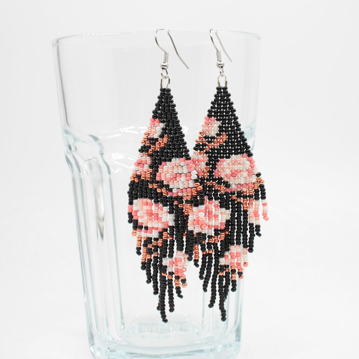 Long beaded seed bead fringe earrings hanging on the rim of drinking class. Base color of these earrings is and black and it has pink roses pattern. Pitkät käsintehdyt roikkuvat helmikorvakorut roikkumassa juomalasin reunalla. Pohjaväri näissä korvakoruissa on musta sekä, kuviona on pinkin sävyisiä ruusuja.