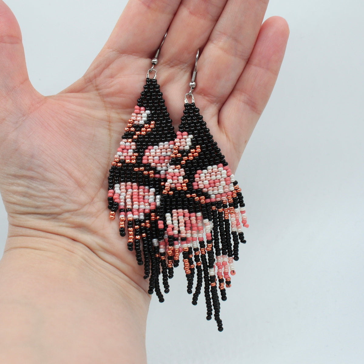 Long beaded seed bead fringe earrings hanging on the hand. Base color of these earrings is and black and it has pink roses pattern. Pitkät käsintehdyt roikkuvat helmikorvakorut roikkumassa kädessä. Pohjaväri näissä korvakoruissa on musta sekä, kuviona on pinkin sävyisiä ruusuja.