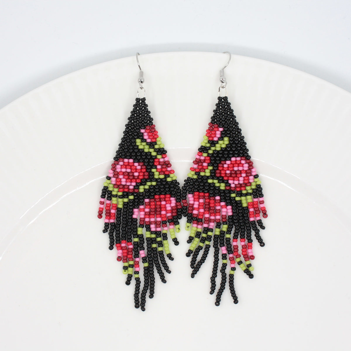 Long beaded seed bead fringe earrings on white plate. Base color of these earrings is and black and it has red roses pattern. Pitkät käsintehdyt roikkuvat helmikorvakorut valkoisella lautasella. Pohjaväri näissä korvakoruissa on musta sekä, kuviona on punaisen sävyisiä ruusuja.
