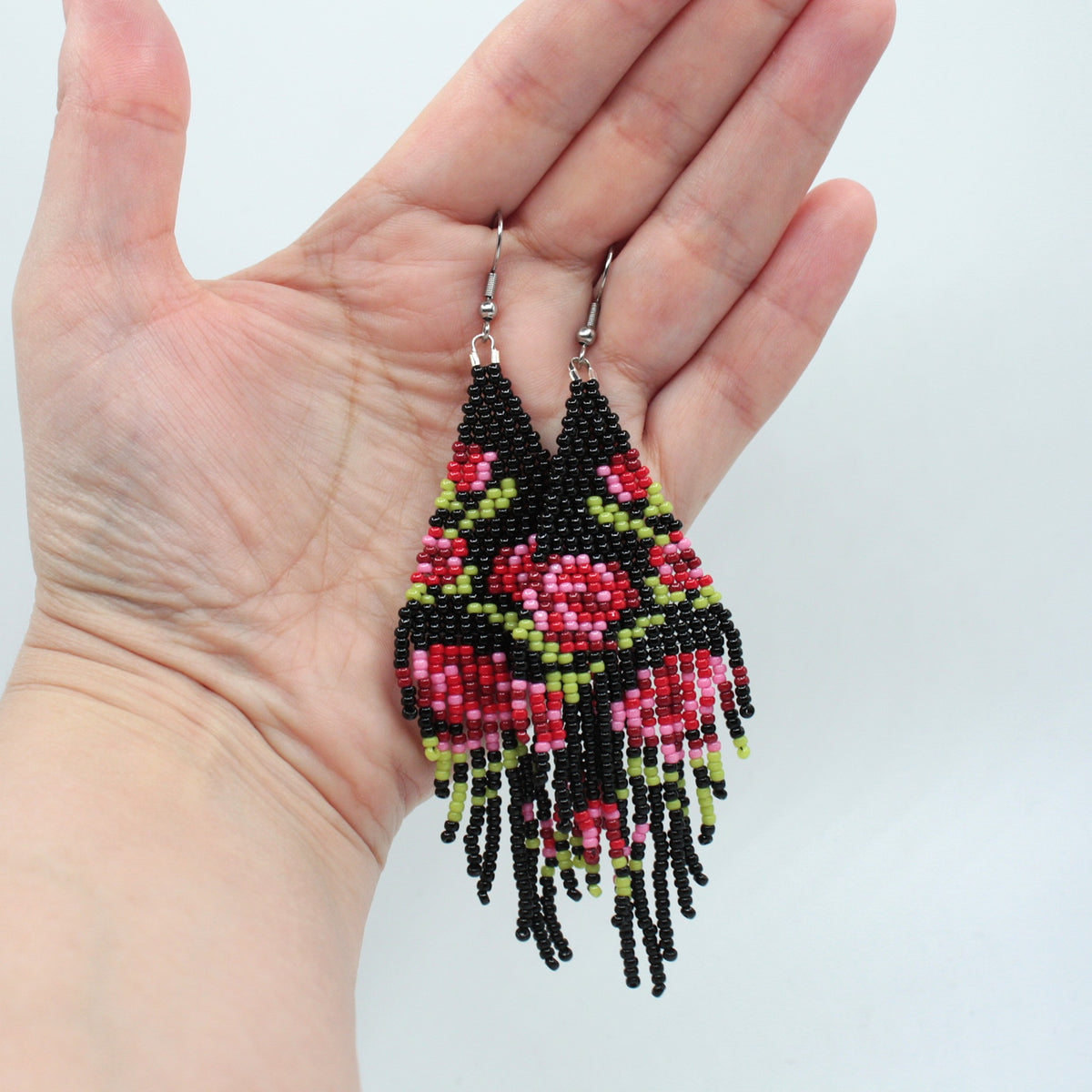 Long beaded seed bead fringe earrings hanging on the hand . Base color of these earrings is and black and it has red roses pattern. Pitkät käsintehdyt roikkuvat helmikorvakorut roikkumassa kädessä. Pohjaväri näissä korvakoruissa on musta sekä, kuviona punaisen eri sävyisiä ruusuja.