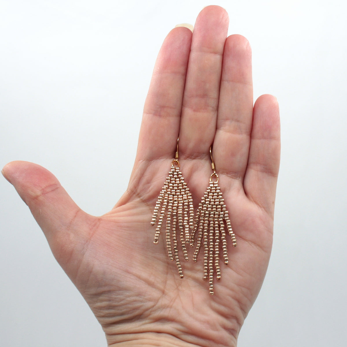 Hapsulliset helmikorvakorut värinä samppanja roikkumassa kädessä. Champagne-colored beaded seed bead fringe earrings hanging from the hand.