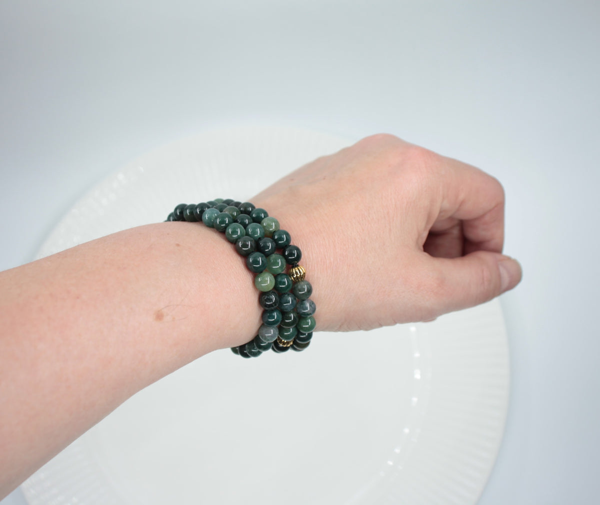 Kolme vihreää sammalakaatti rannekorua kullanvärisellä metallihelmellä. Tausta on valkoinen ja korut ovat ranteessa. Three green moss agate bracelet with gold color metal bead. Background is white and bracelet are on the wrist.