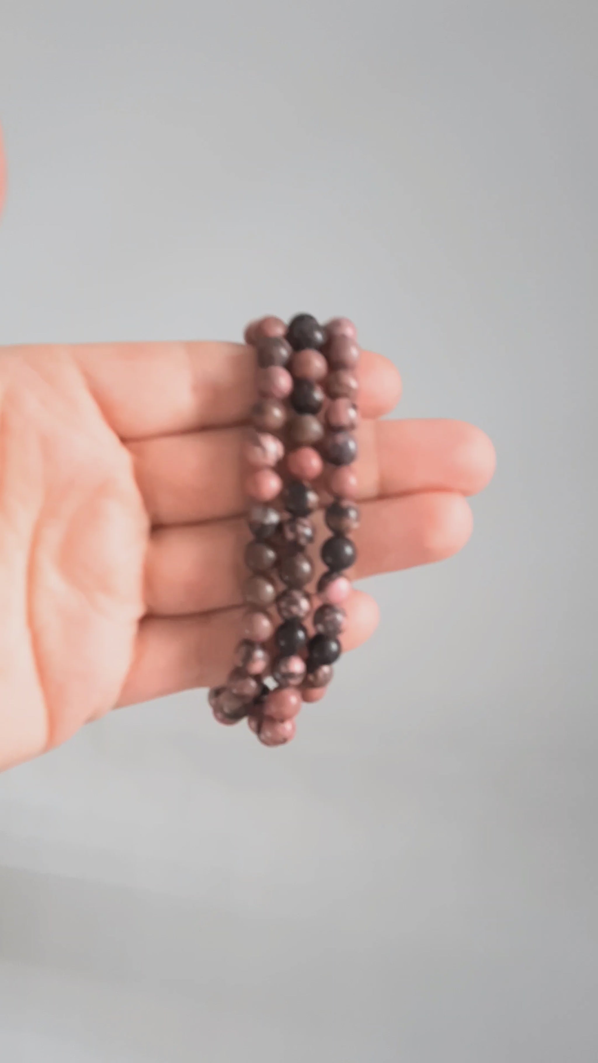 Kolme rodoniitti rannekorua esittelyssä kädessä. Three rhodonite bracelets in the spotlight on the hand.
