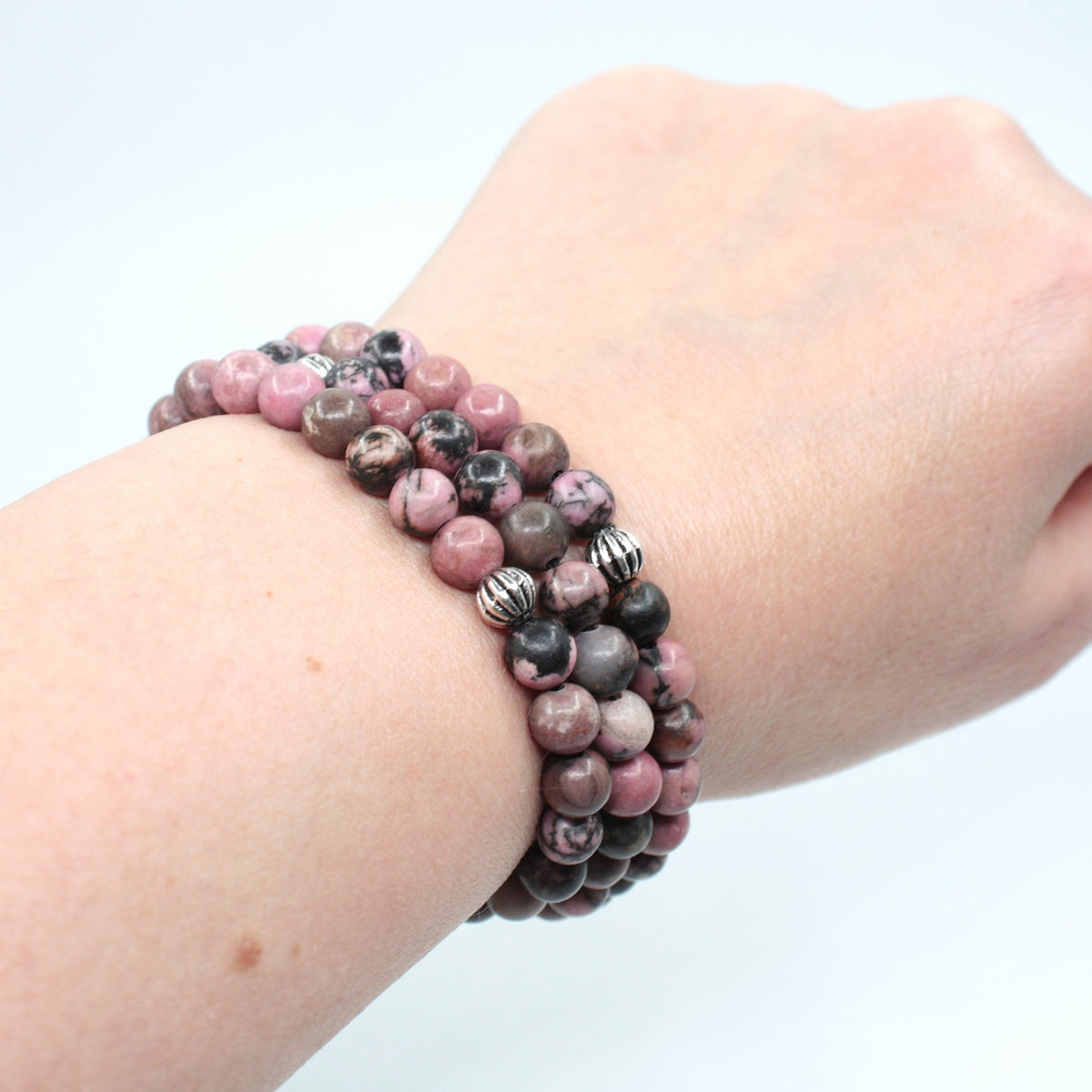Kolme rodoniitti rannekorua ranteessa. Tausta on valkoinen. Three rhodonite bracelets on the wrist. Background is white.