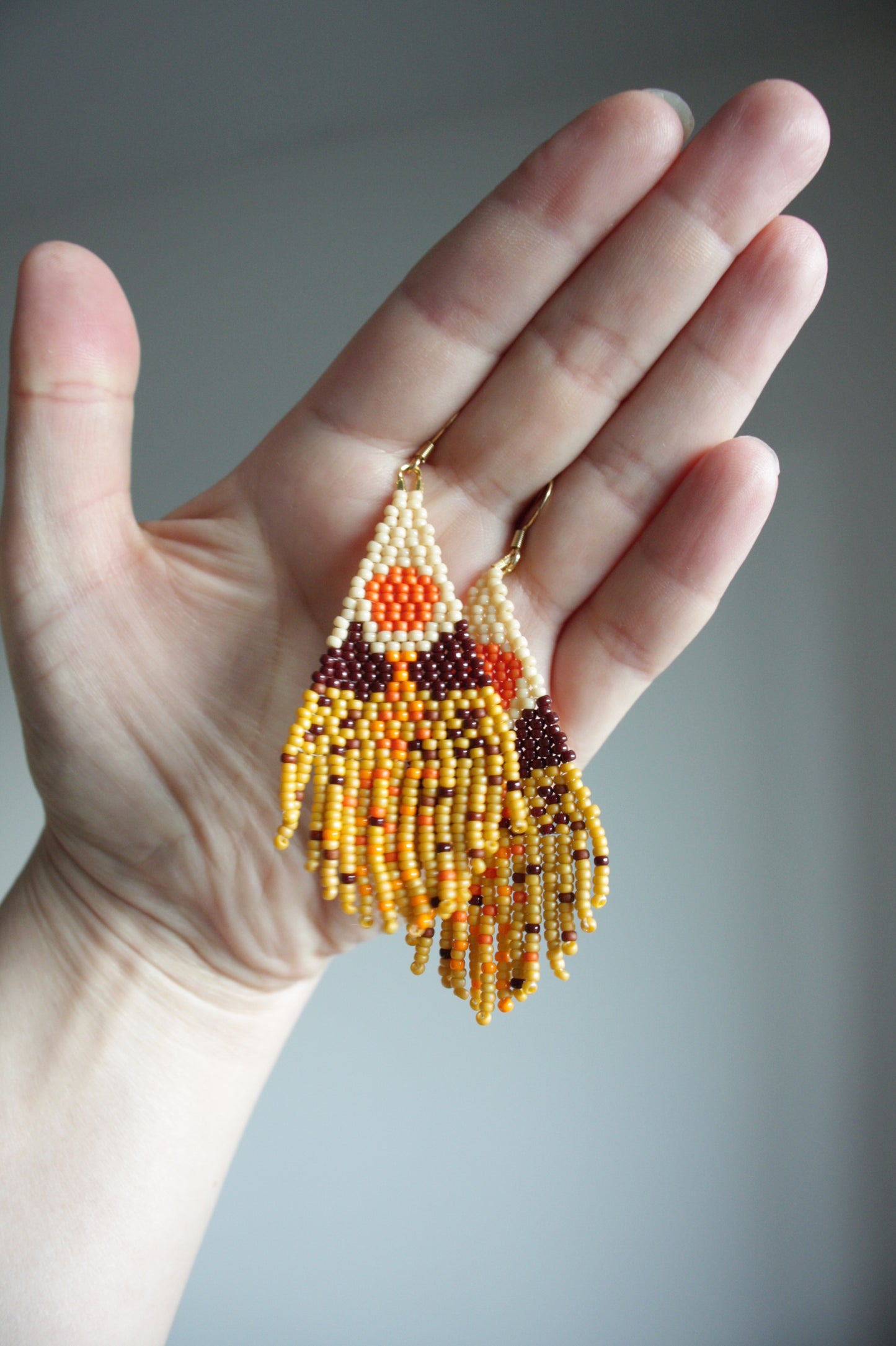 Seed bead fringe earrings with scenery pattern. Colors are brown, yellow and orange shades. Roikkuvat hapsukorvakorut pienistä lasihelmistä. Kuviona näissä korvakoruina on maisema ja värit loistavat keltaisen, ruskean ja oranssin sävyissä.