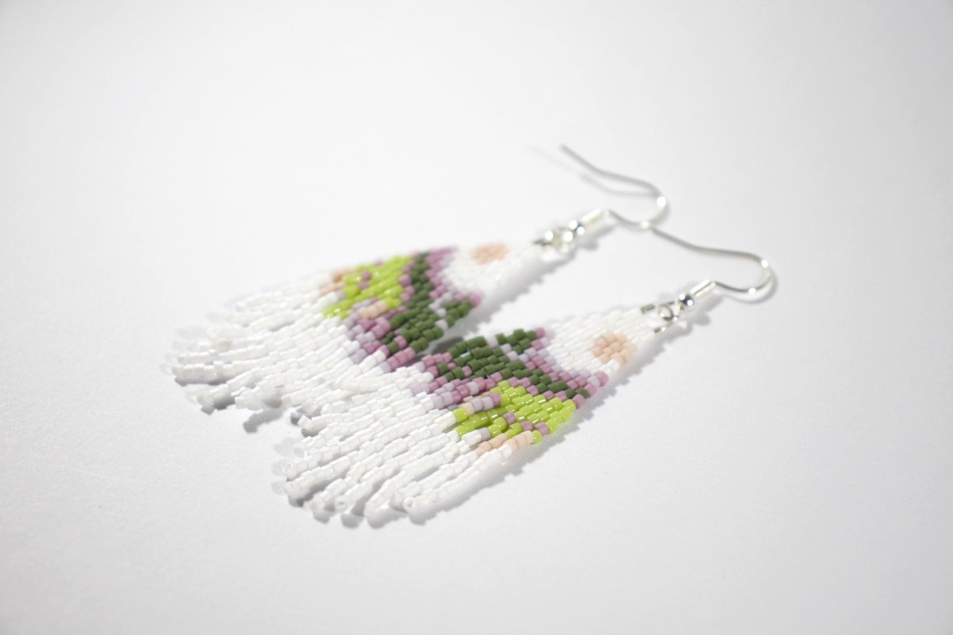Colorful seed bead fringe earrings with landscape pattern. These earrings has white base color. Roikkuvat värikkäät lasihelmi korvakorut maisemakuviolla. Näissä koruissa on valkoinen pohjaväri.