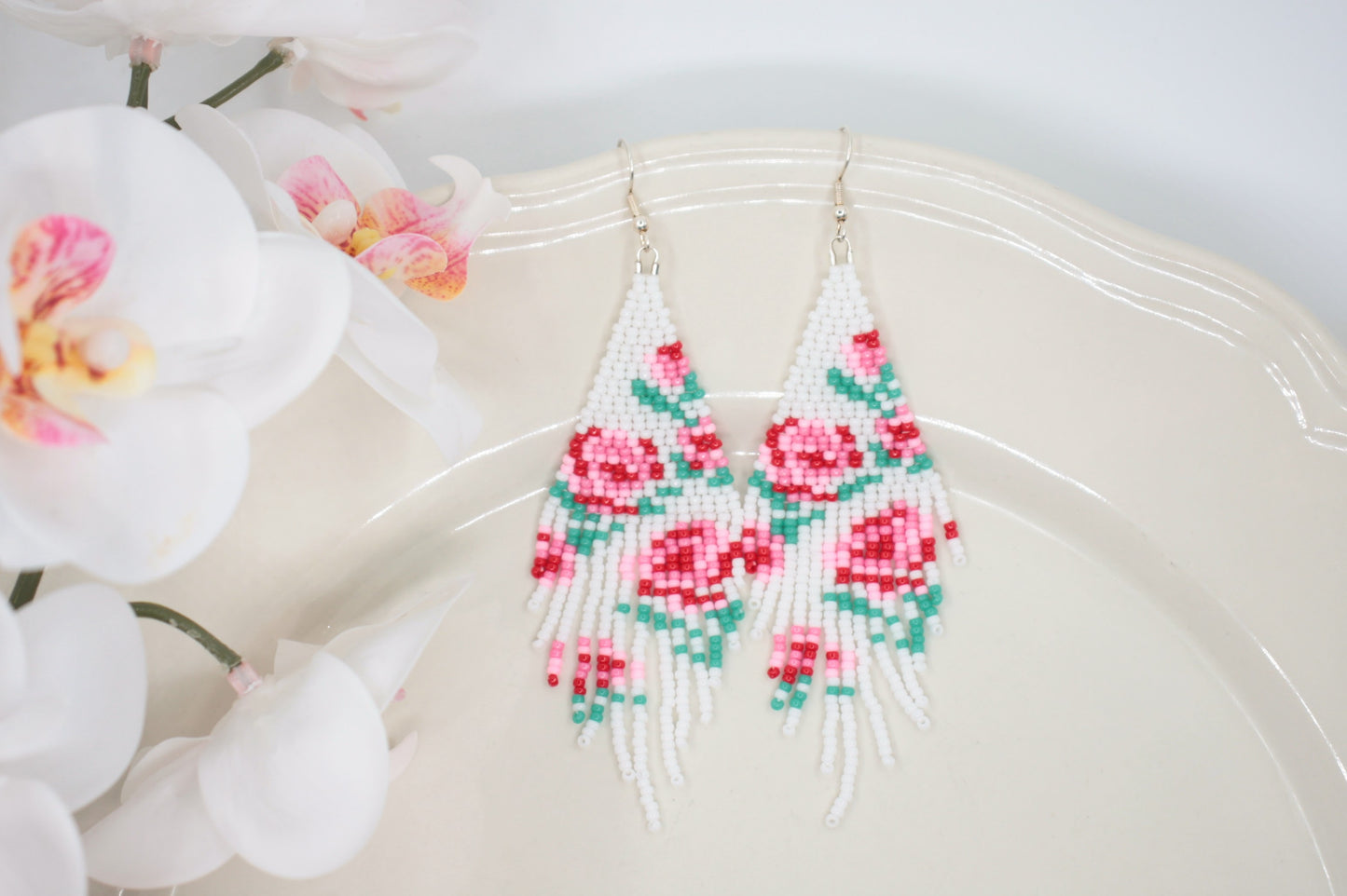 Long beaded seed bead fringe earrings. Base color of these earrings is white and has red and pink roses pattern. Pitkät käsintehdyt roikkuvat helmikorvakorut. Pohjaväri näissä korvakoruissa on valkoinen sekä, kuviona on punaisia ja pinkkejä ruusuja.  
