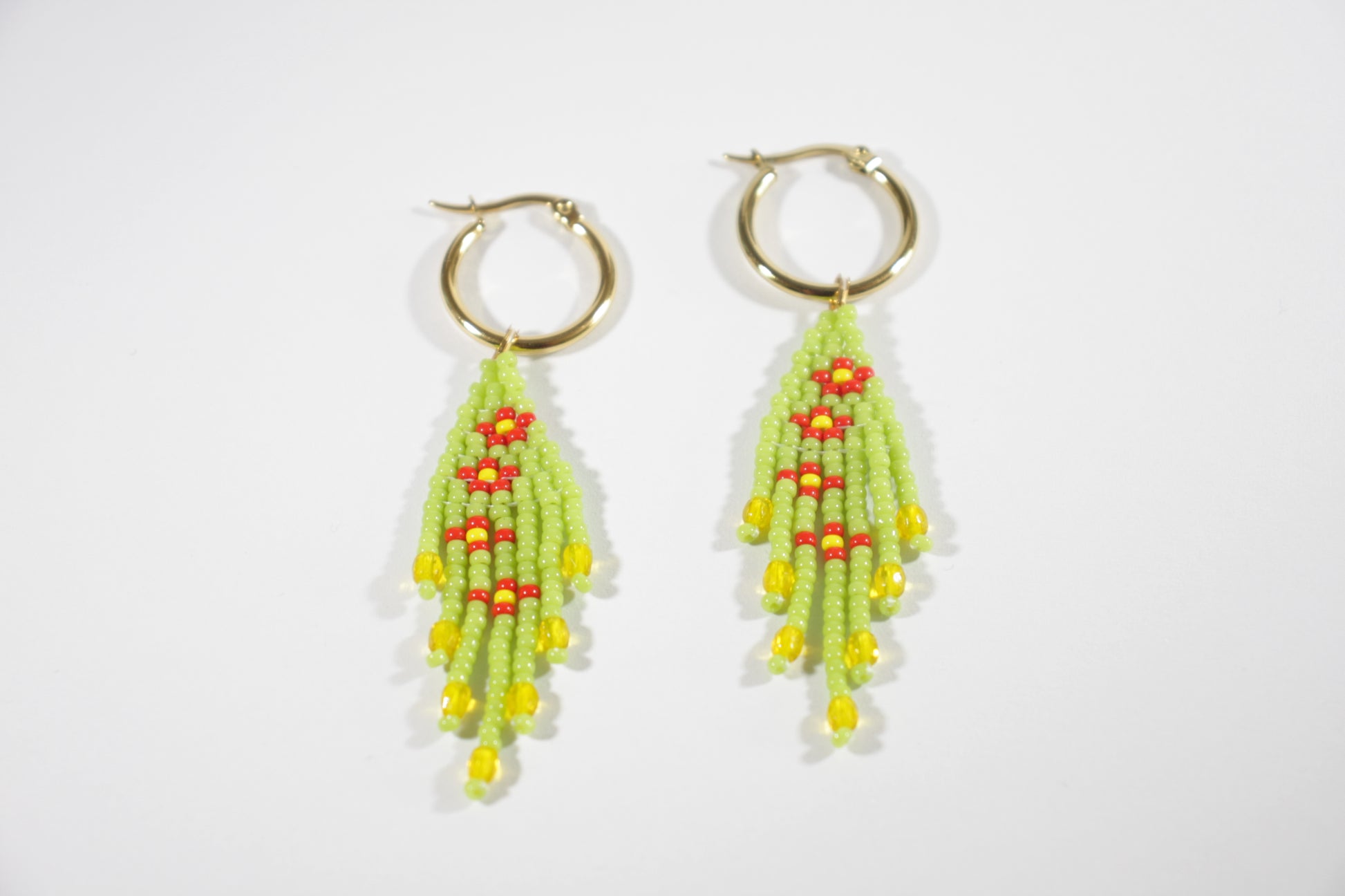 Small fringe seed bead earrings daisies. Color is green and daisies flowers are red with yellow center. Earrings hoops are gold plated stainless steel. Pienet hapsulliset lasihelmikorvakorut kukka kuviolla. Väri on vihreä ja kukat oat punaisia ja niiden keskusta on keltainen. Korvakorurenkaat ovat kullattua ruostumatonta terästä.