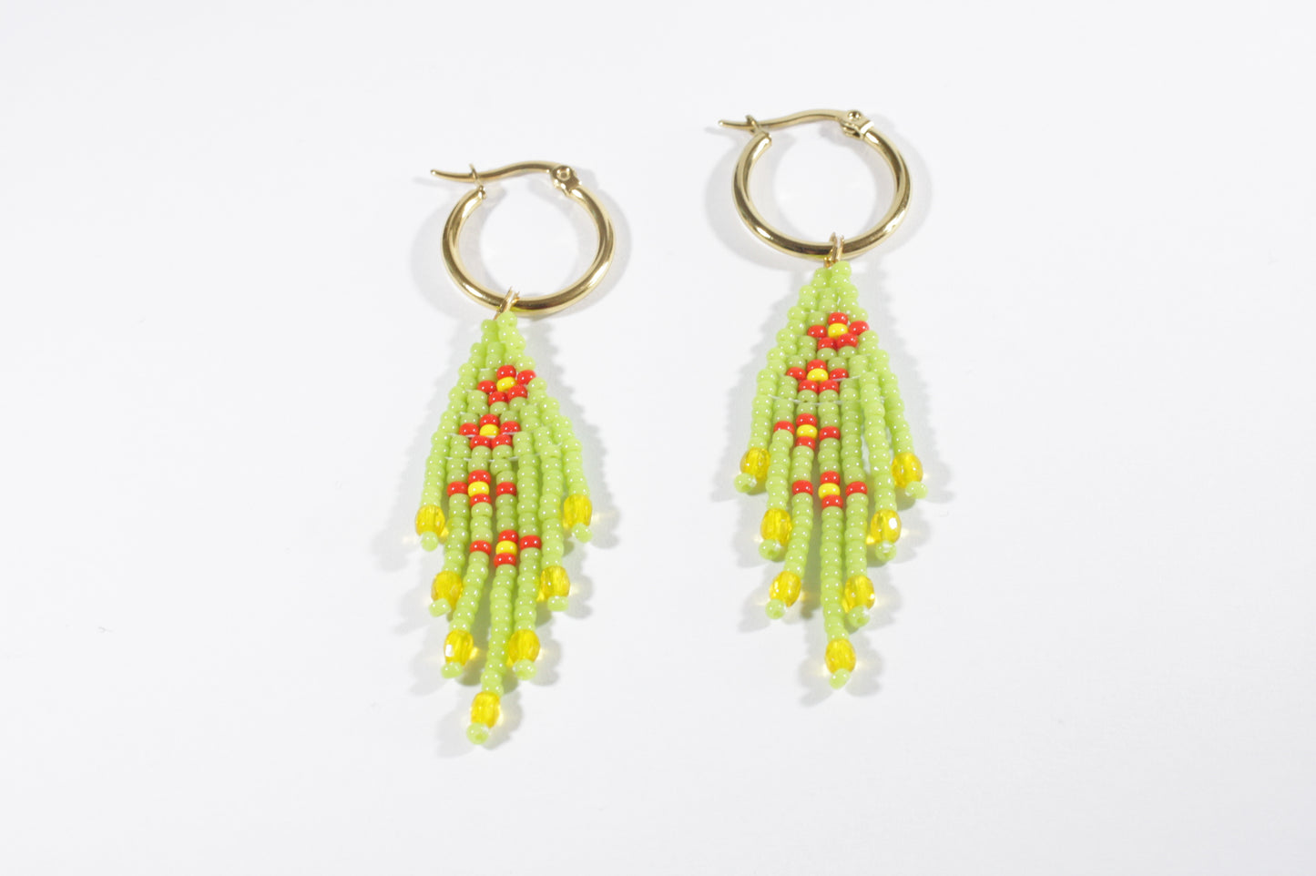 Small fringe seed bead earrings daisies. Color is green and daisies flowers are red with yellow center. Earrings hoops are gold plated stainless steel. Pienet hapsulliset lasihelmikorvakorut kukka kuviolla. Väri on vihreä ja kukat oat punaisia ja niiden keskusta on keltainen. Korvakorurenkaat ovat kullattua ruostumatonta terästä.