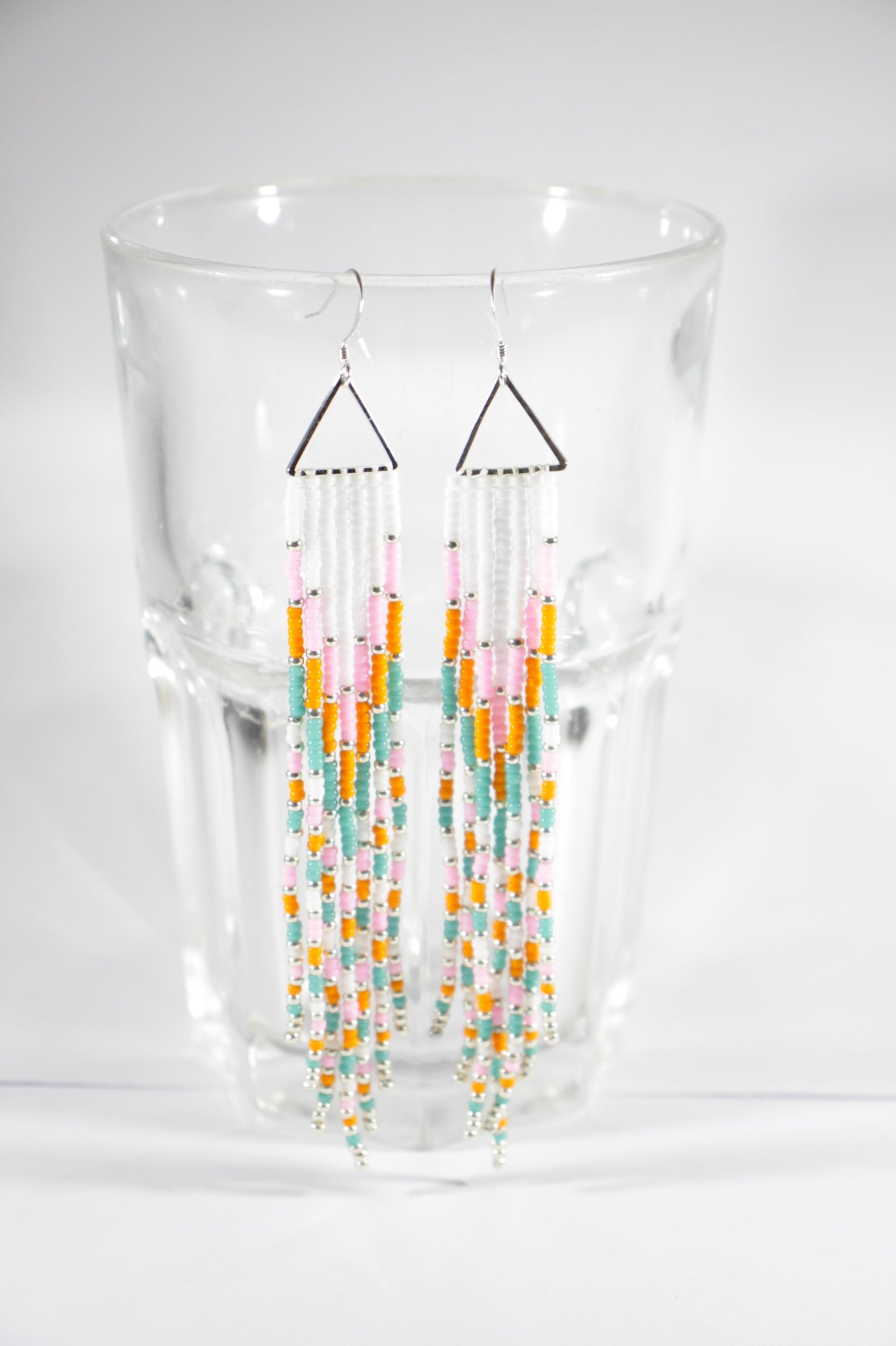 Long fringe seed bead earrings with silver color triangle links and hooks. Fringe color are white, pink, orange and turquoise with silver color beads in between.