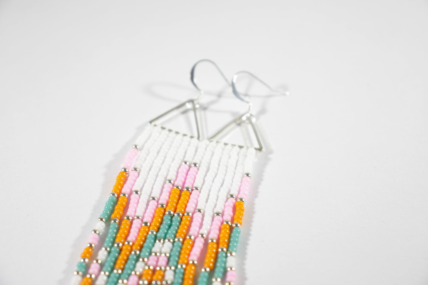 Long fringe seed bead earrings with silver color triangle links and hooks. Fringe color are white, pink, orange and turquoise with silver color beads in between.