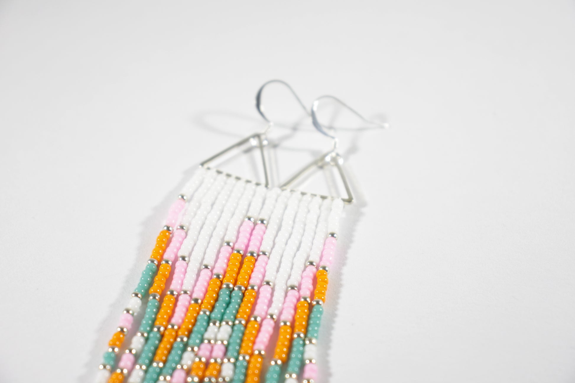 Long fringe seed bead earrings with silver color triangle links and hooks. Fringe color are white, pink, orange and turquoise with silver color beads in between.