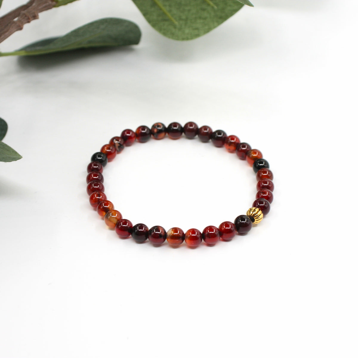 Ruskean sävyinen unelma-akaatti rannekoru valkoisella alustalla. Taustalla näkyy hieman vihreitä lehtiä. 
A brown-toned Dream Agate bracelet on a white surface. There is a little bit green leaves in the background.