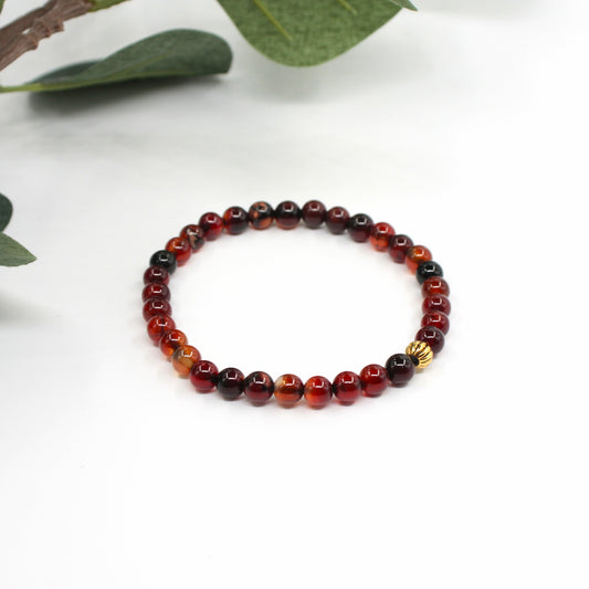 Ruskean sävyinen unelma-akaatti rannekoru valkoisella alustalla. Taustalla näkyy hieman vihreitä lehtiä. 
A brown-toned Dream Agate bracelet on a white surface. There is a little bit green leaves in the background.