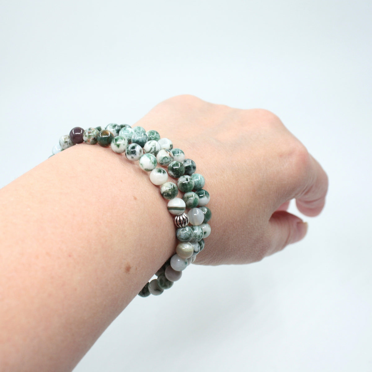 Kolme puu-akaatti rannekorua ranteessa. Tausta on valkoinen. Three wood agate bracelets on the wrist. Background is white