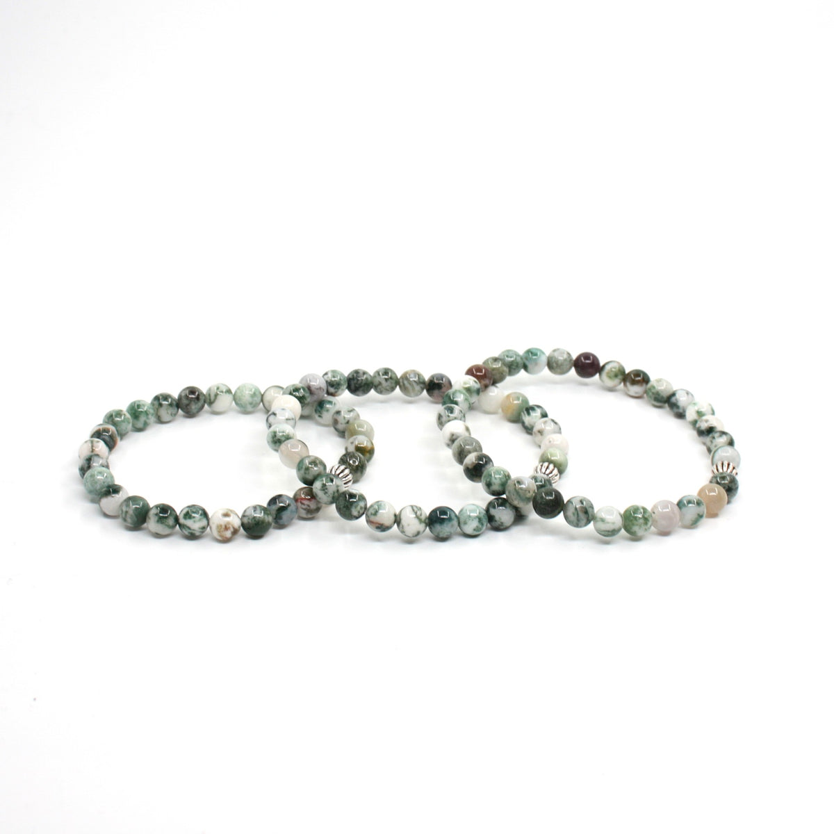 Kolme puu-akaatti rannekorua valkoisella alustalla. Three rhodonite bracelets on the white surface.